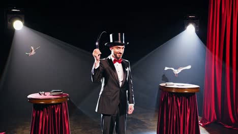 a magician in a tuxedo and top hat performs on stage with red curtains and spotlights