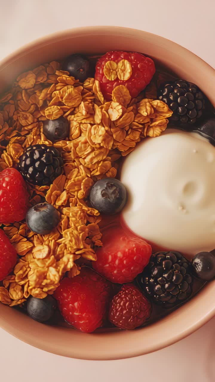 Vertical video: Moving camera revealing pink bowl on tabletop, showcasing granola yogurt berries