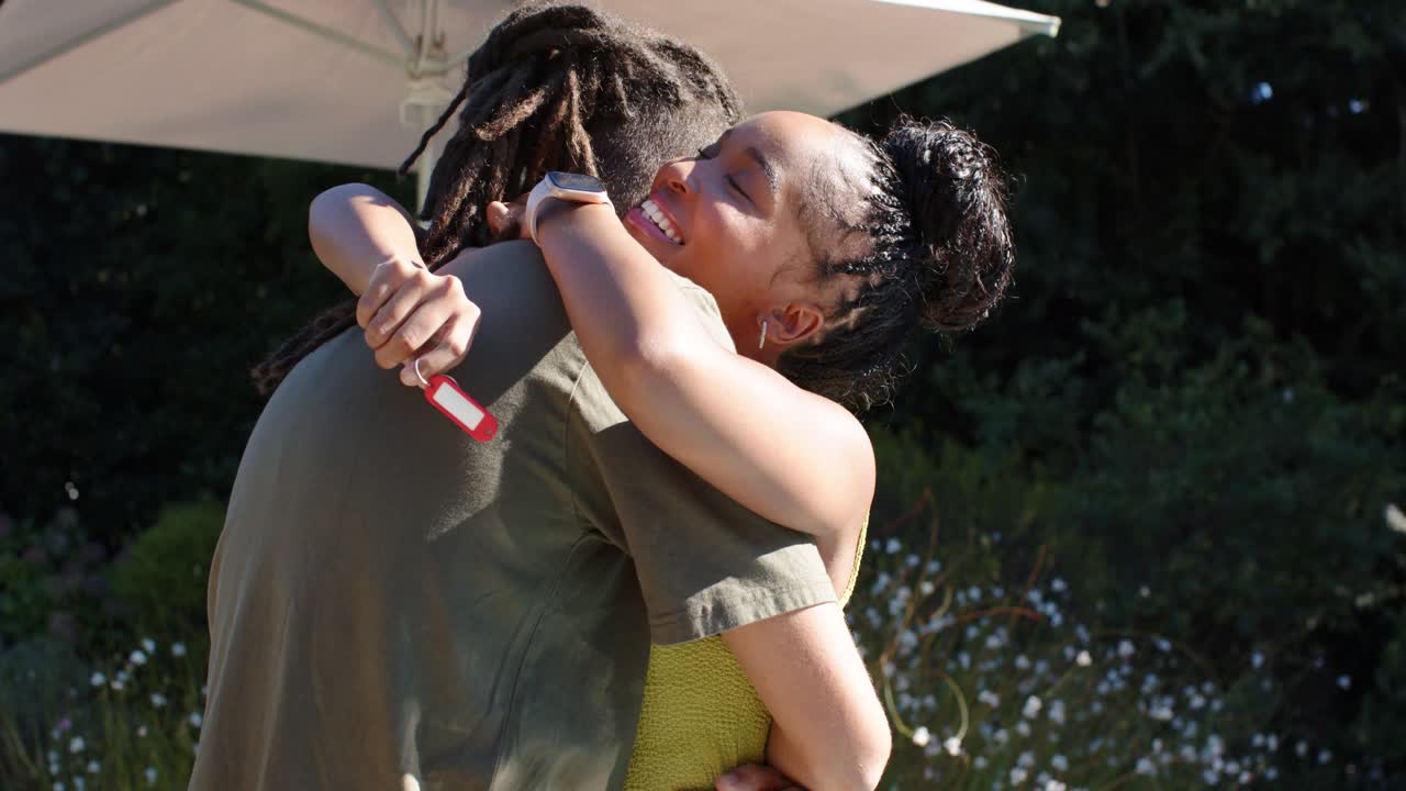African American couple hugging tighter in sunny garden after woman showing red key fob, smiling