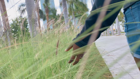 african american woman walking in park touching tall grass
