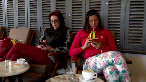 mujeres se sientan en una cafetería y usan teléfonos inteligentes