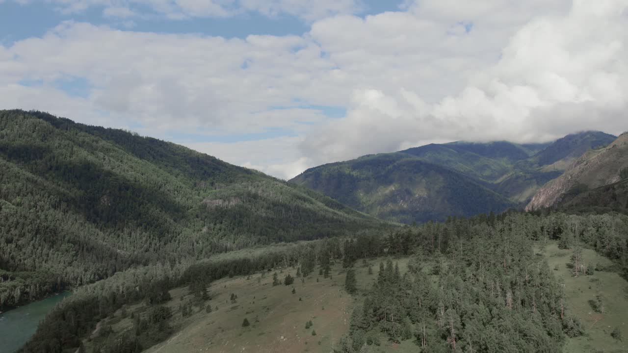 Riprese aeree con drone della Valle di Ak-Kem nei Monti Altai, Russia, che mostrano versanti collinari boscosi, un fiume serpeggiante e un cielo nuvoloso imponente su una natura selvaggia remota.