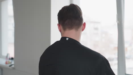 young man in black jacket walks toward window while pushing suitcase handle inward, blur of outdoor scene through window in background