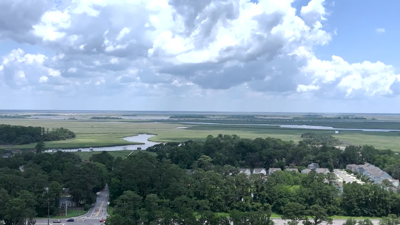 Drone orbit of Wilmington Island neighborhoods with Tybee bridge in view and small private pond, daylight aerial of coastal Georgia residential scenery.
