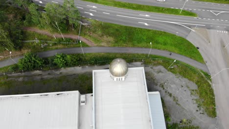 Gold-dome-cupola-and-ornate-cross-on-top-of-roof-of-church-in-abandoned-lot-by-asphalt-street-and-green-trees-on-sunny-day,-overhead-aerial