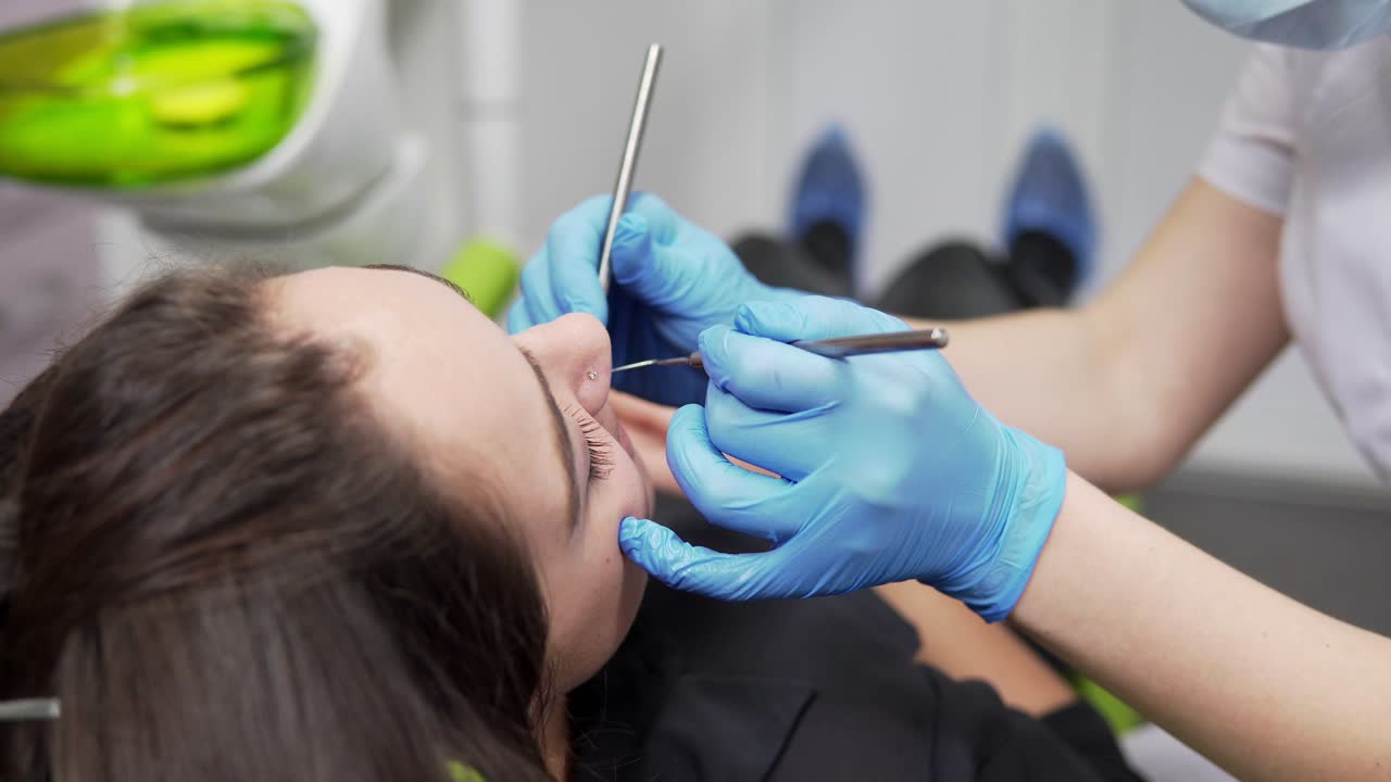 Young female dentist is examining patient's teeth. Closeup view of female dentist's hands in gloves holding the instruments. Healthy teeth and dental healthcare.