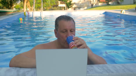 Hombre-Sonriente-En-La-Piscina-De-Su-Casa-Con-Una-Computadora-Portátil