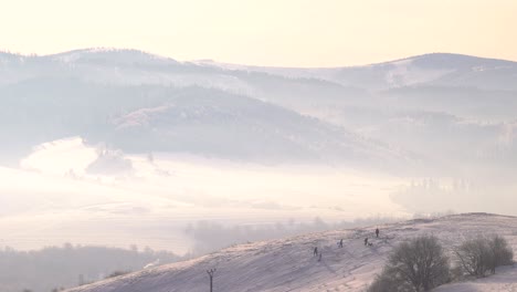 silhouette of family with dog playing on snowy winter hill against mountain backdrop