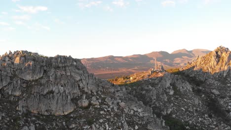 una toma de dron inclinada que captura el paisaje rocoso y las líneas eléctricas de la cima de una montaña al atardecer