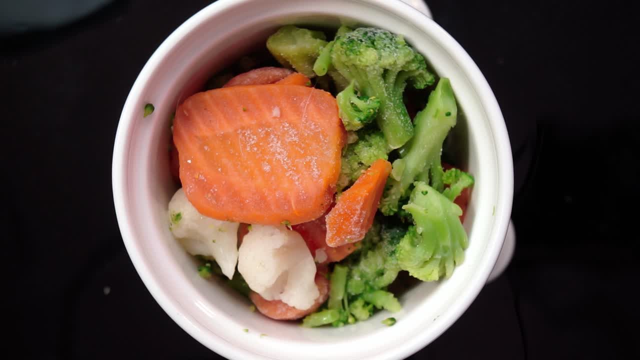 Bowl of frozen vegetables rotating over a dark background, cinematic soft light and vibrant color detail