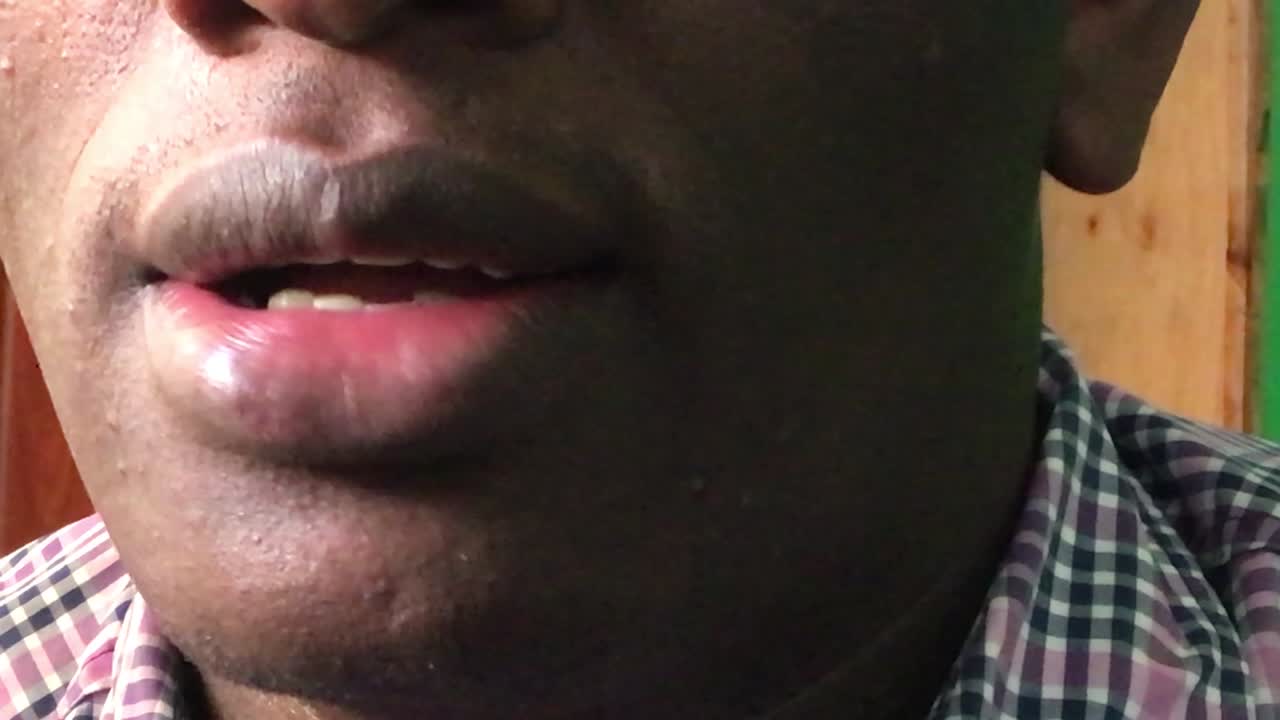 Macro shot of african male person smiling with lips inside lighting studio. Showing tooth into camera.