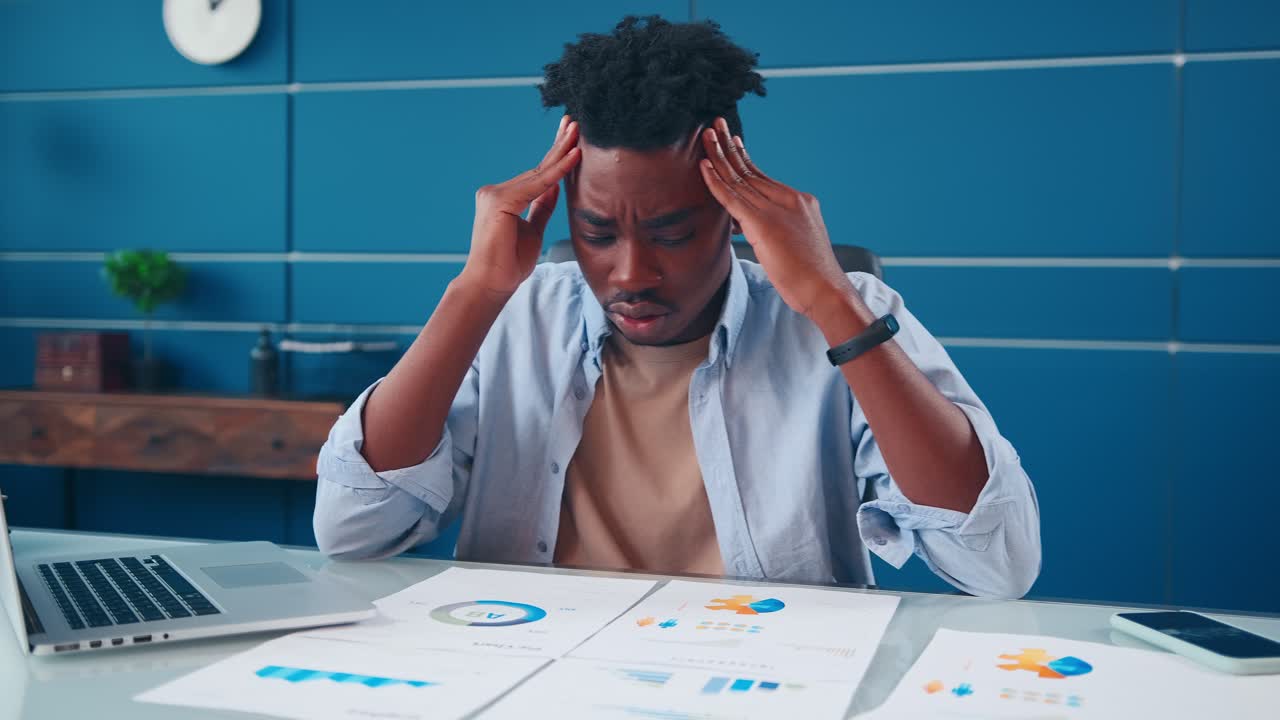 Young african american man holding head anxious about seeing financial charts