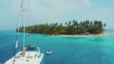 sailboat floating near a beautiful tropical island with palm tree forest by the caribbean sea