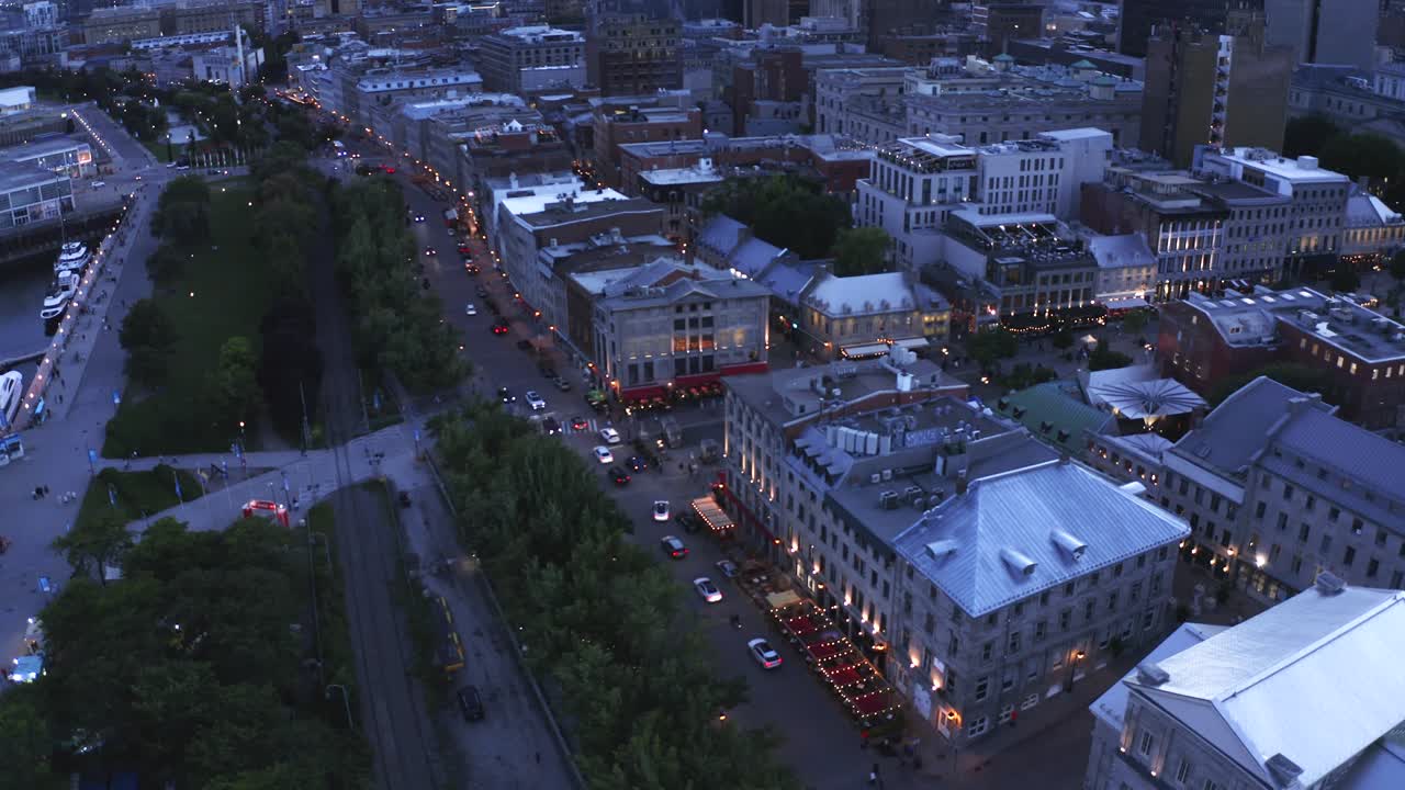 Aerial shot over Montreal's Old Port at dusk, with the city lights reflecting on the water and the Ferris wheel glowing. Captures the serene beauty and vibrant atmosphere of the evening.