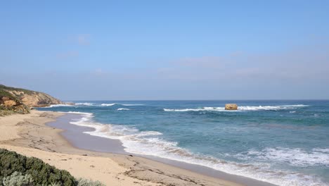 waves crashing on sandy beach with rocky cliffs