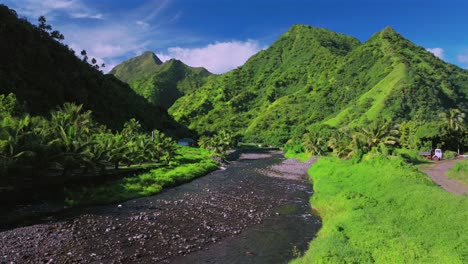 Mountain-valley-river-coconut-trees-Teahupoo-Tahiti-aerial-drone-French-Polynesia-South-Pacific-island-bright-afternoon-sunny-green-lush-blue-sky-clouds-WSL-surfing-Olympic-venue-end-of-road-backwards