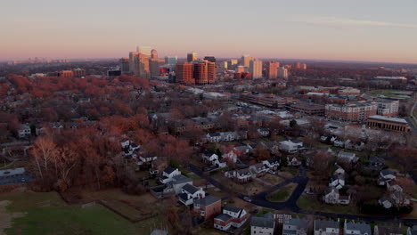 pull away from a downtown city skyline at sunset to reveal neighborhood houses and a soccer practice on a football field