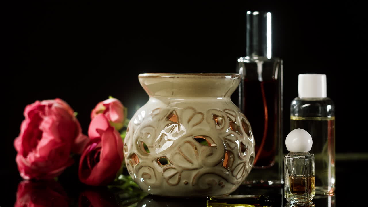 Main plaçant un flacon de parfum à côté d’un diffuseur d’arômes et de fleurs