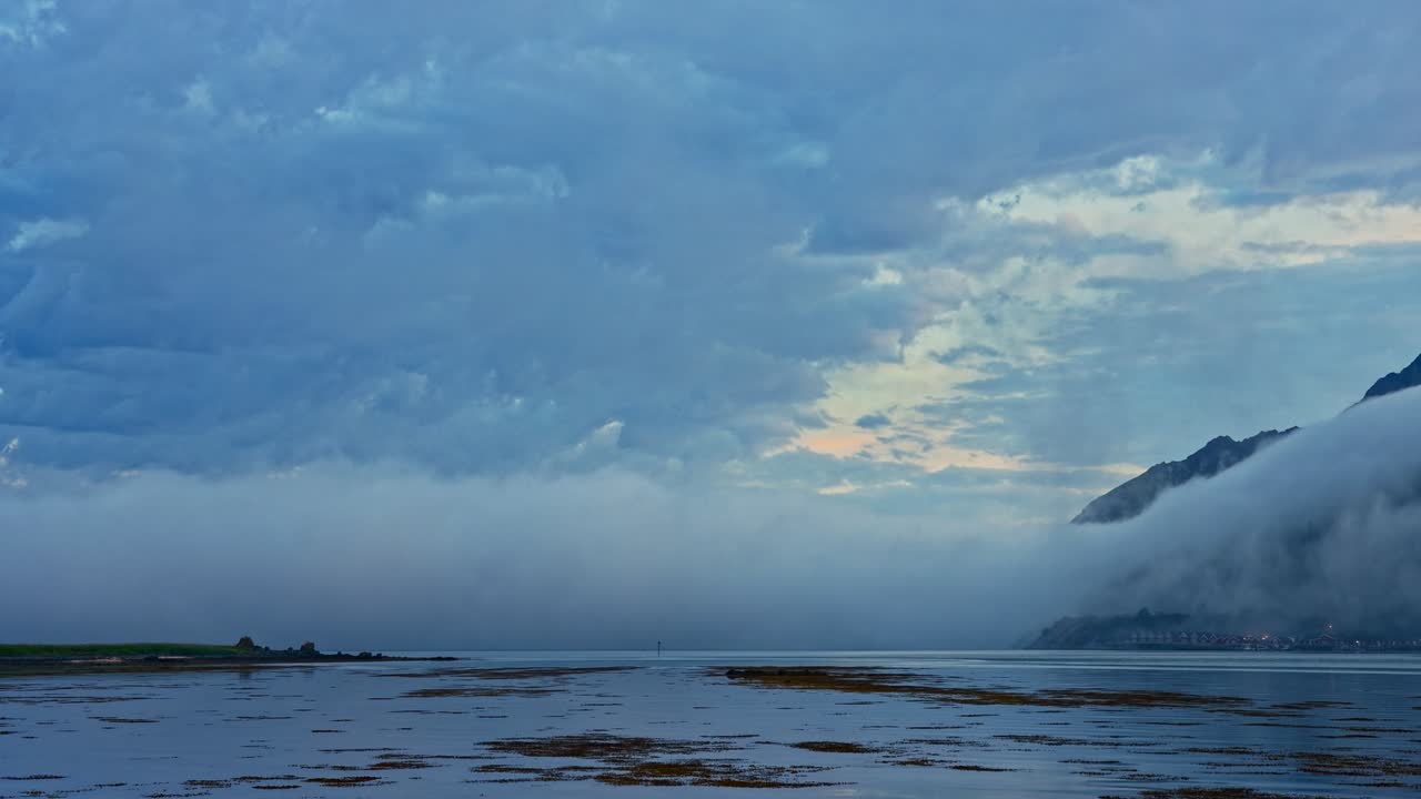 Panning Time Lapse. Clouds and thick sea fog over coastal mountains on a bright arctic summer night during low tide. Lofoten Islands, Northern Norway