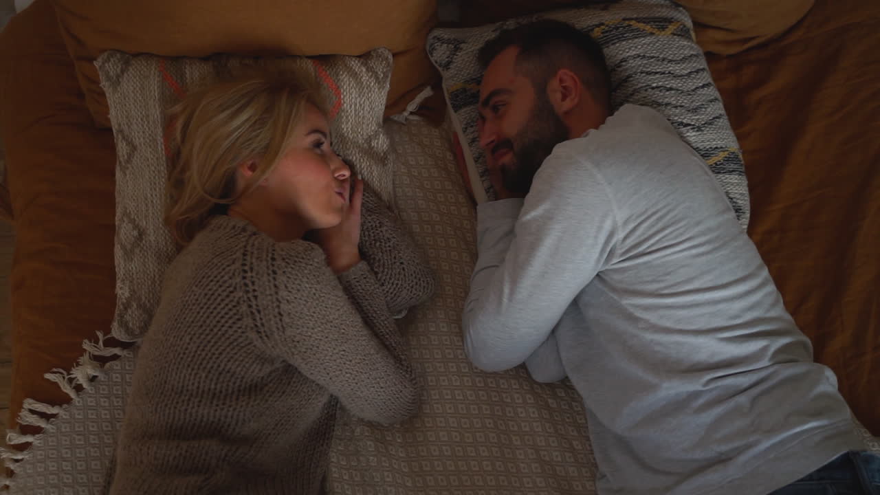 una pareja encantadora acostada en la cama mirándose, teniendo una conversación romántica cara a cara en un día de invierno