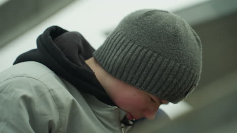 close-up of a young boy wearing a gray jacket and green beanie, deeply focused on a task near an iron railing, he looks frustrated