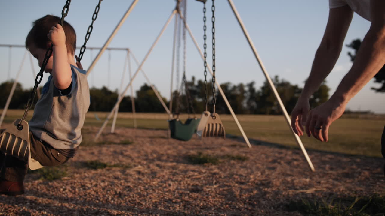 un padre y un hijo felices jugando afuera en el parque en el columpio al atardecer en cámara lenta cinematográfica
