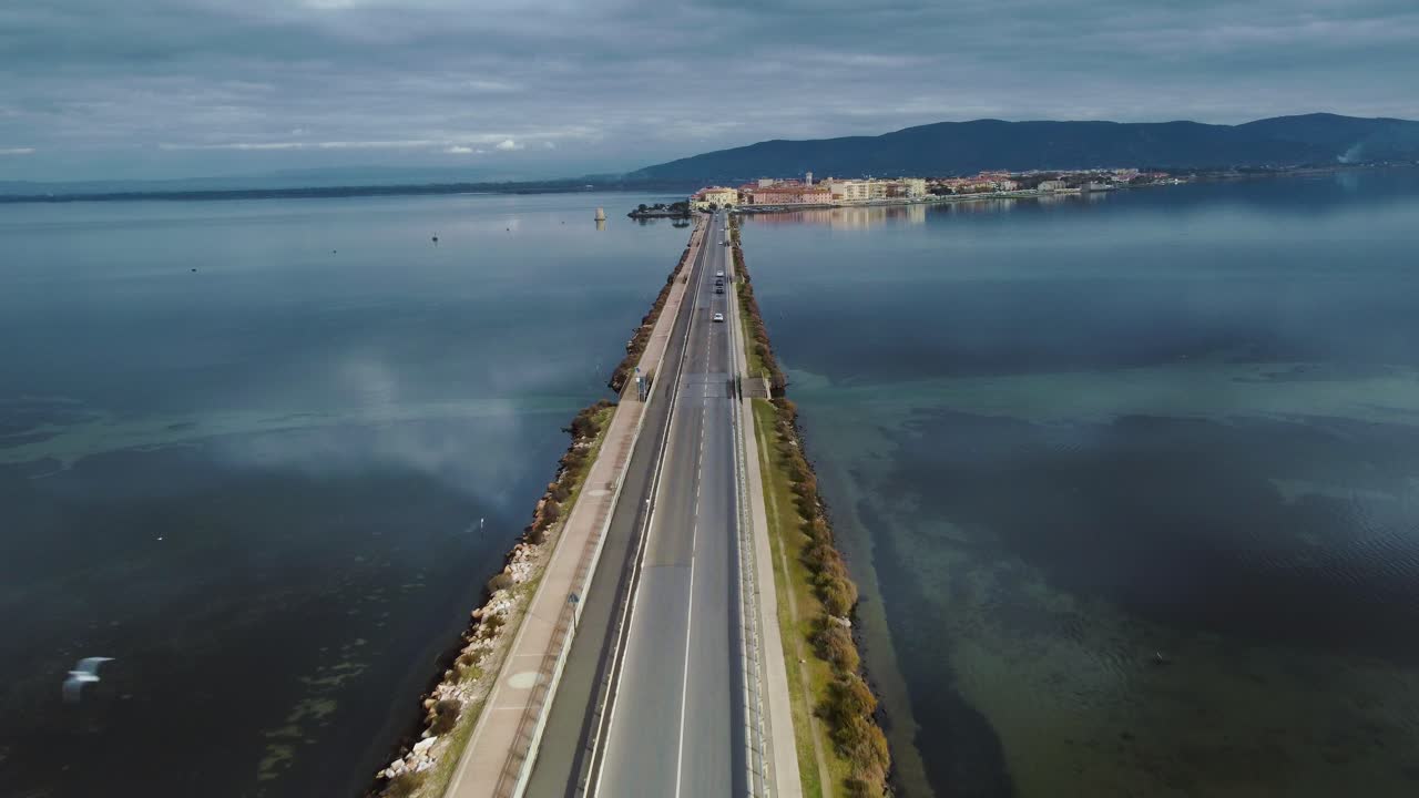 мостовая дорога через лагуну в направлении старого островного города орбетелло недалеко от монте-арджентарио и природного парка маремма в тоскане, италия, с голубым небом и спокойной голубой водой