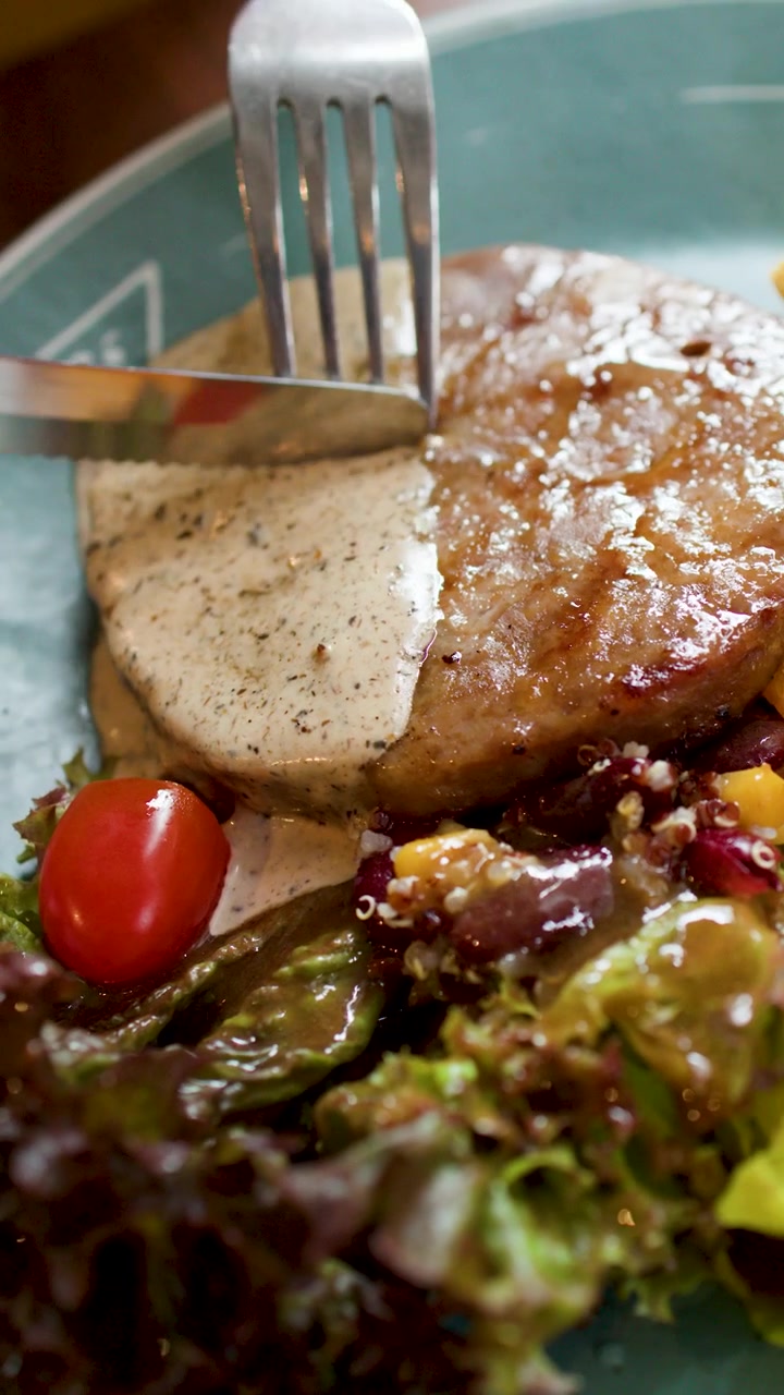 Una persona usa coltello e forchetta per tagliare una bistecca alla griglia con salsa cremosa.
