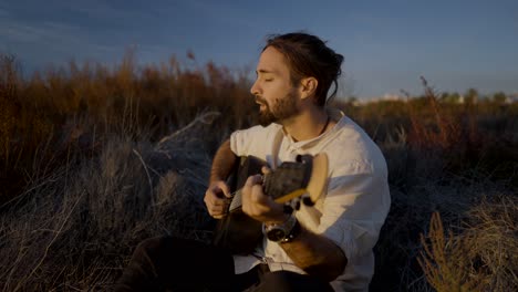 man playing guitar in a field at sunset