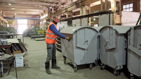 industrial plant inside. worker puts ready garbage bins on the factory. interior of manufacturing.