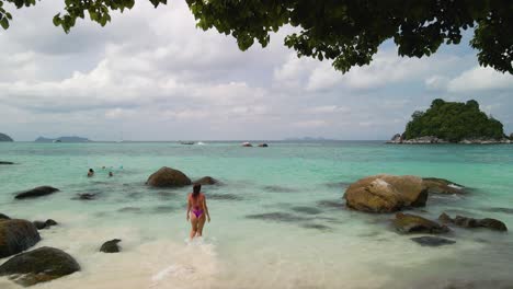 Low-flying-aerial-follow-shot-of-a-woman-walking-into-the-ocean-before-overtaking-her-and-flying-out-to-sea