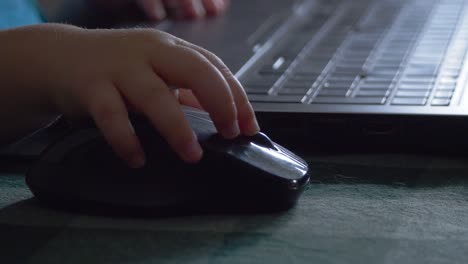 pequeña mano del niño haciendo clic en el ratón del portátil, por la ventana de primer plano