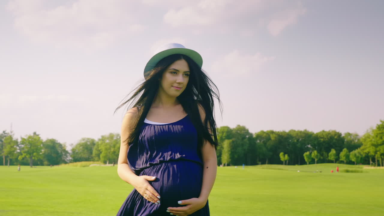 스테디캠 샷:젊은 임산부가 푸른 초원을 걷고 있다