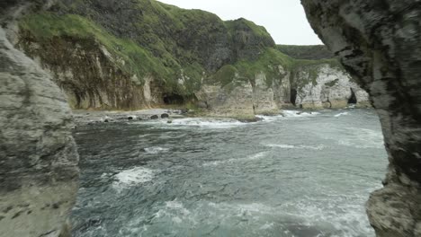 drone flying through coastal white cliff arch on a cloudy day in county antrim, northern ireland