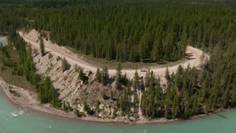 Toma-De-Drone-De-Una-Camioneta-Conduciendo-Hacia-El-Desierto-Del-Parque-Nacional-De-Kootenay-En-Un-Camino-Forestal-Junto-Al-Río-Kootenay