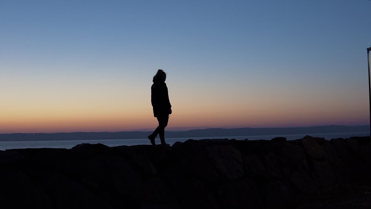 una silueta de una niña caminando sobre rocas durante la hora azul