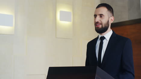 close-up view of caucasian businessman wearing formal clothes on a podium and speaking at a conference in front of many people