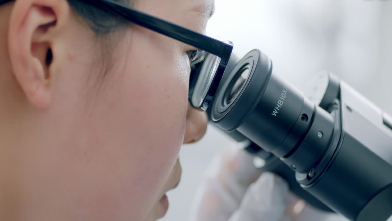 Smart female biologist looking into the microscope, Analyzes Petri Dish Sample. Specialist Working on Medicine, Biotechnology Research in Advanced Pharma Lab for detection of antibodies and infections