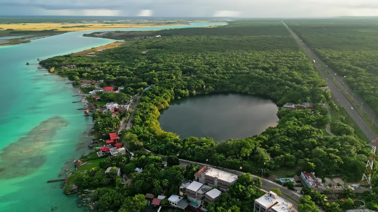 Aerial footage of a large circular cenote and turquoise lagoon near Bacalar, Quintana Roo, Mexico. Winding waters, lush shoreline, and tropical serenity in a stunning natural scene