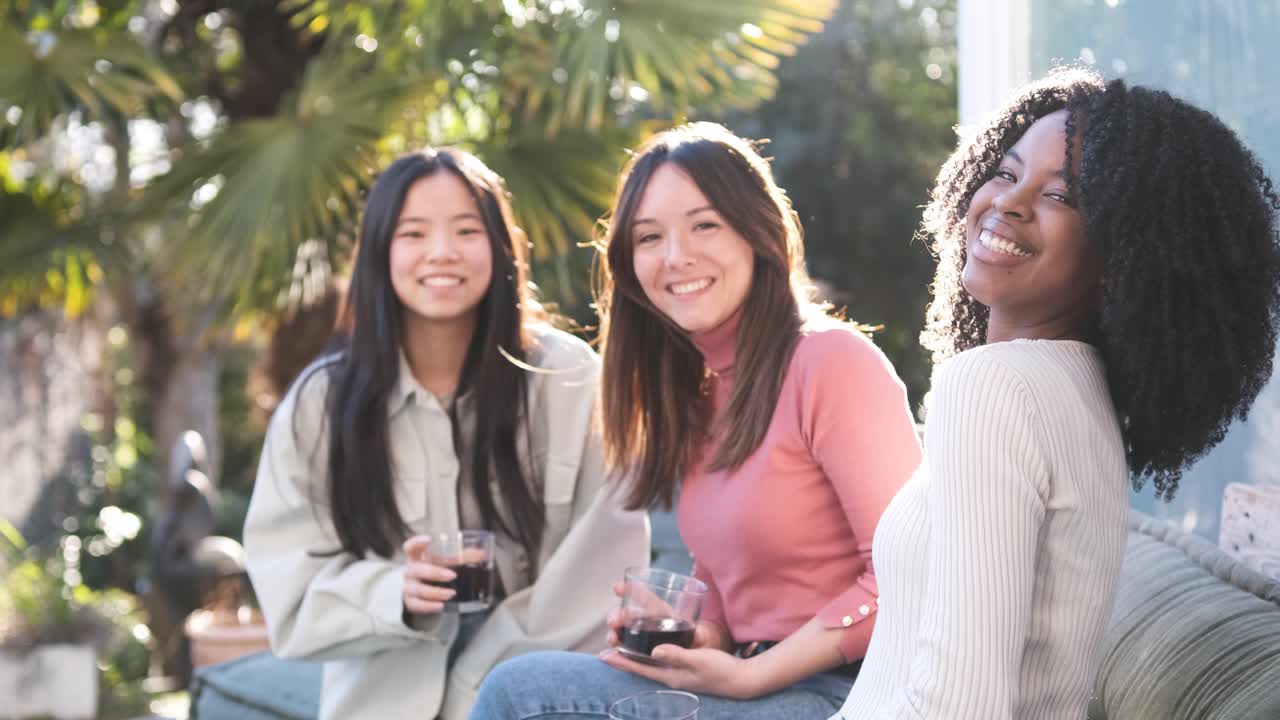 Diverse girlfriends drinking beverages on terrace