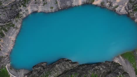 Ascending-aerial-view-of-blue-water-lake-formed-in-the-deep-sinkhole-completely-surrounded-by-tall-cliffs-in-Imotski,-Croatia