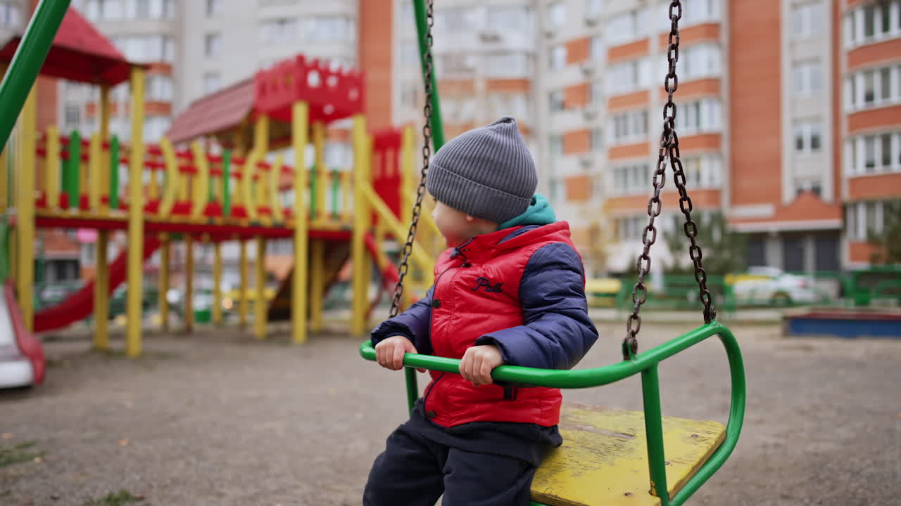 Sweet baby boy sitting on the swing in the playground. Little kid outdoors in the yard.