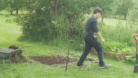 young male gardener tipping wheelbarrow tending to garden