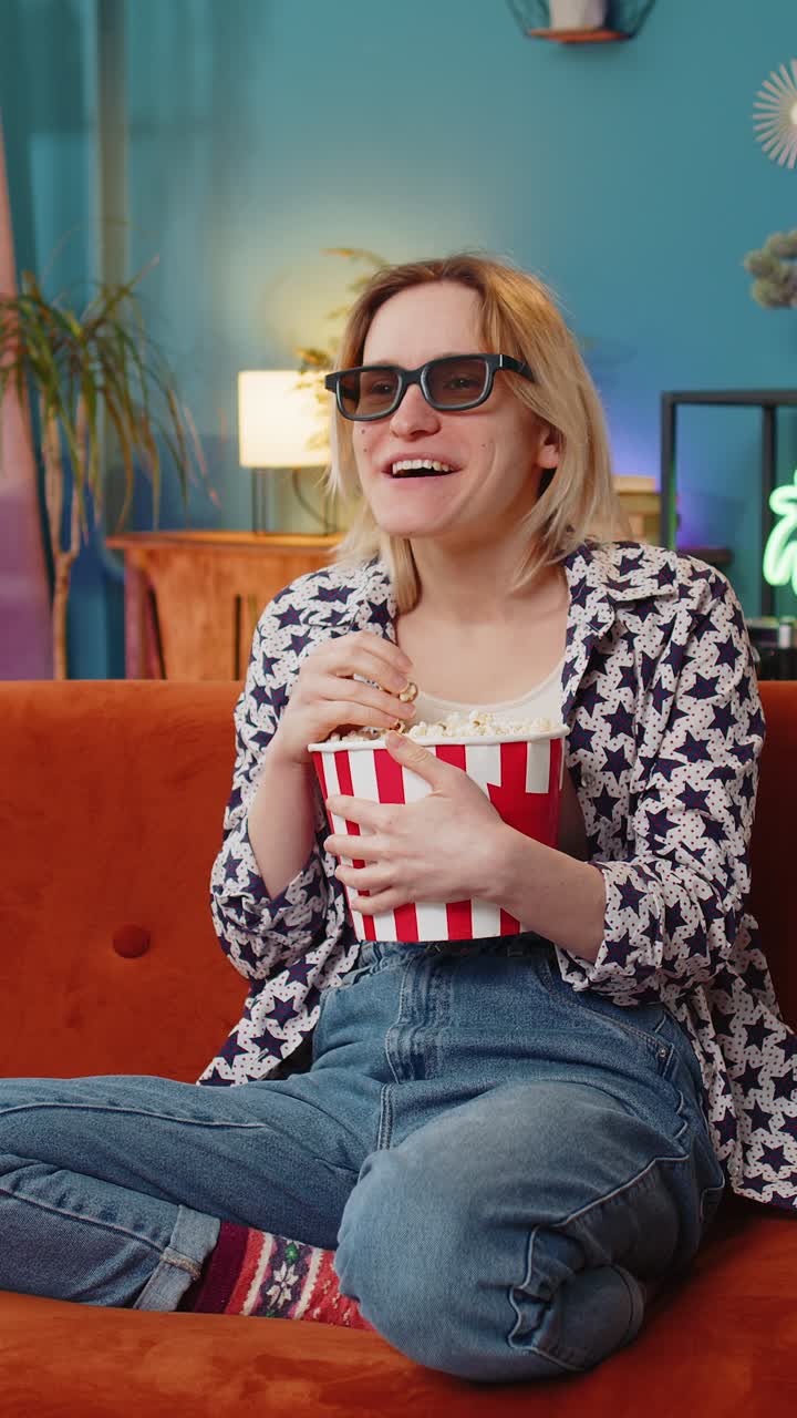joven emocionada sentada en el sofá comiendo palomitas de maíz y viendo un interesante juego de serie de televisión