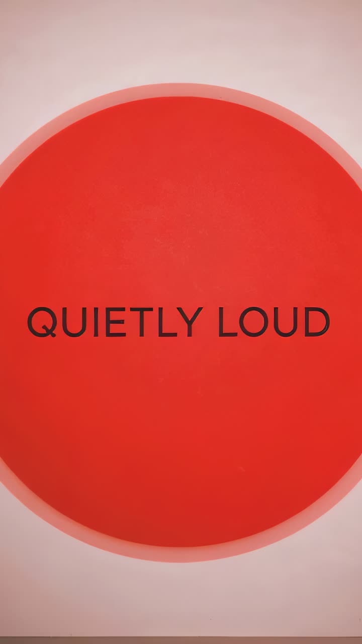 Video verticale: riproduzione di una sequenza, disco rosso che si sposta a destra su una parete color crema, con il testo QUIETLY LOUD