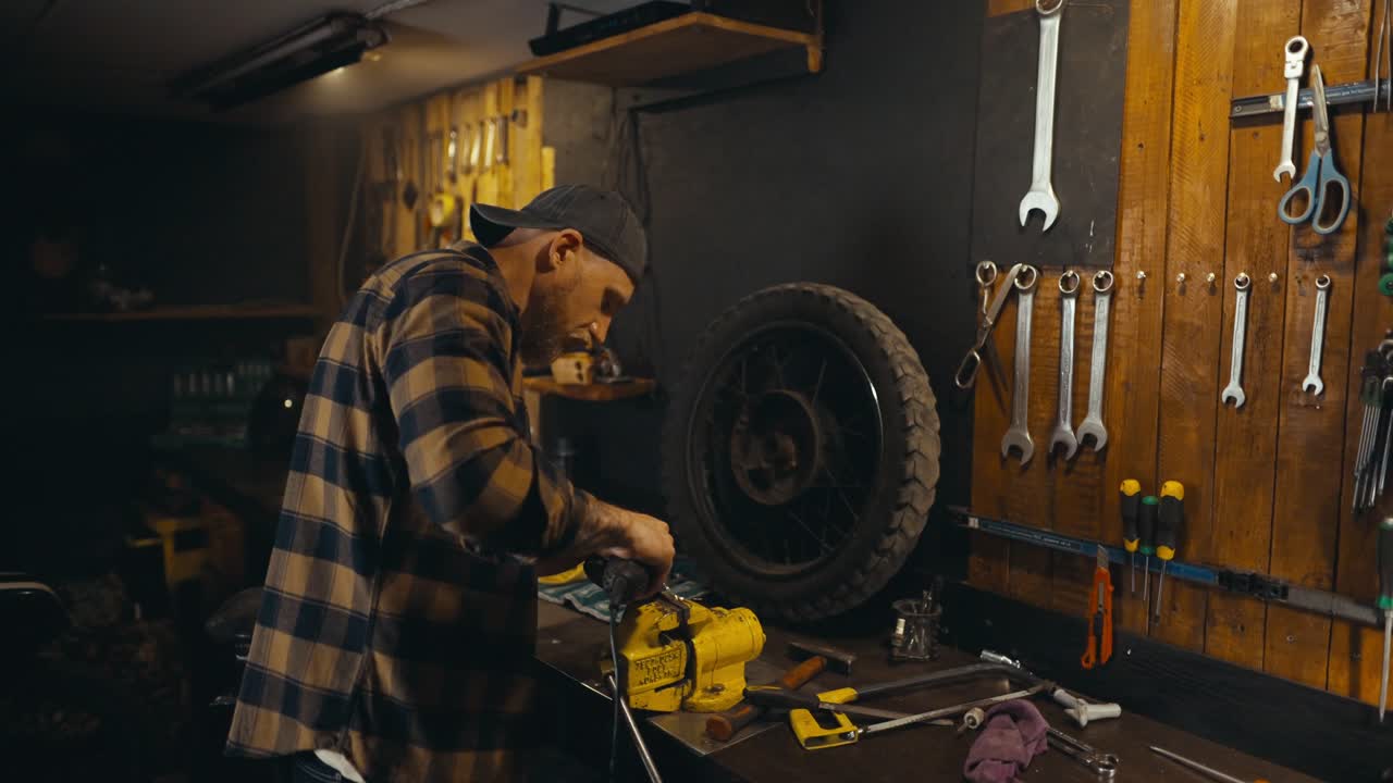 Confident guy mechanic works on a workbench and polishes a metal part creating bright sparks in a studio workshop