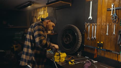 confident guy mechanic works on a workbench and polishes a metal part creating bright sparks in a studio workshop