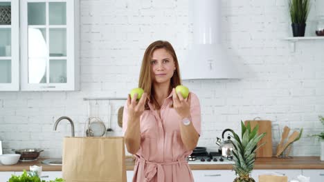 a girl in a white kitchen near a grocery bag holds green apples in her hands