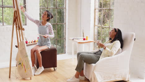 multiracial young woman painting on canvas while grandmother relaxes with coffee at home