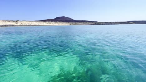 crystal clear ocean water with volcano in the background and white sand beach, baja california sur, mexico